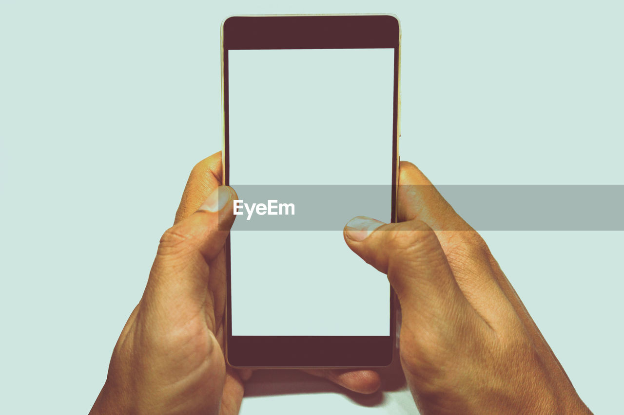 Cropped hands holding mobile phone against white background