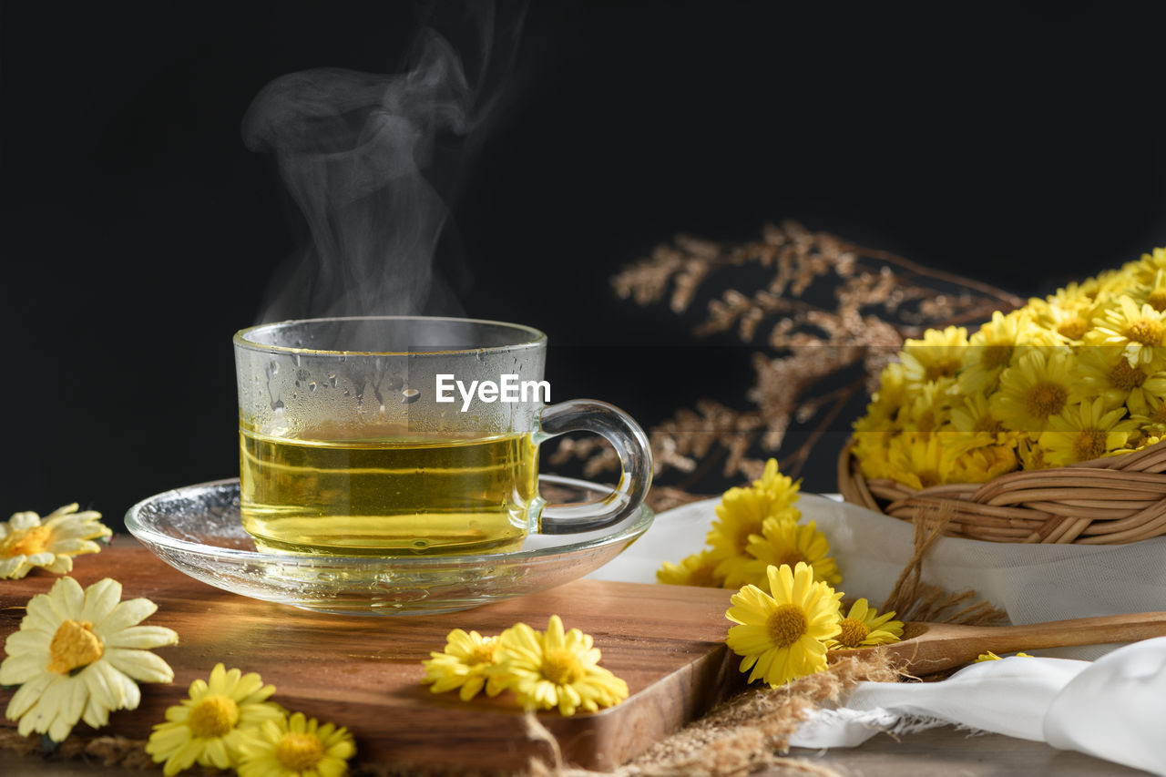 Chrysanthemum tea with hot steam and chrysanthemum flower in basket on black background. 