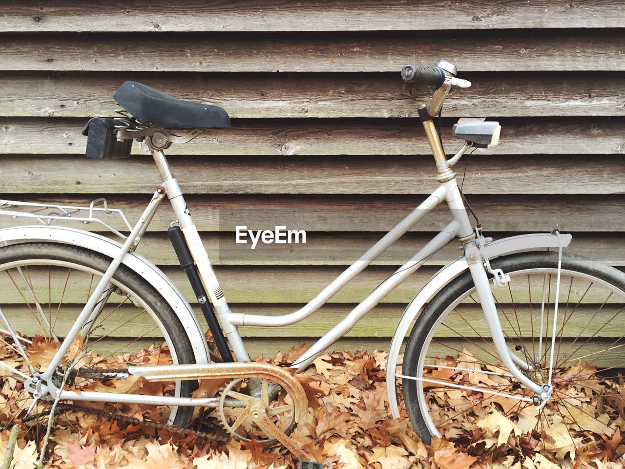 Bicycle parked on fallen autumn leaves against fence