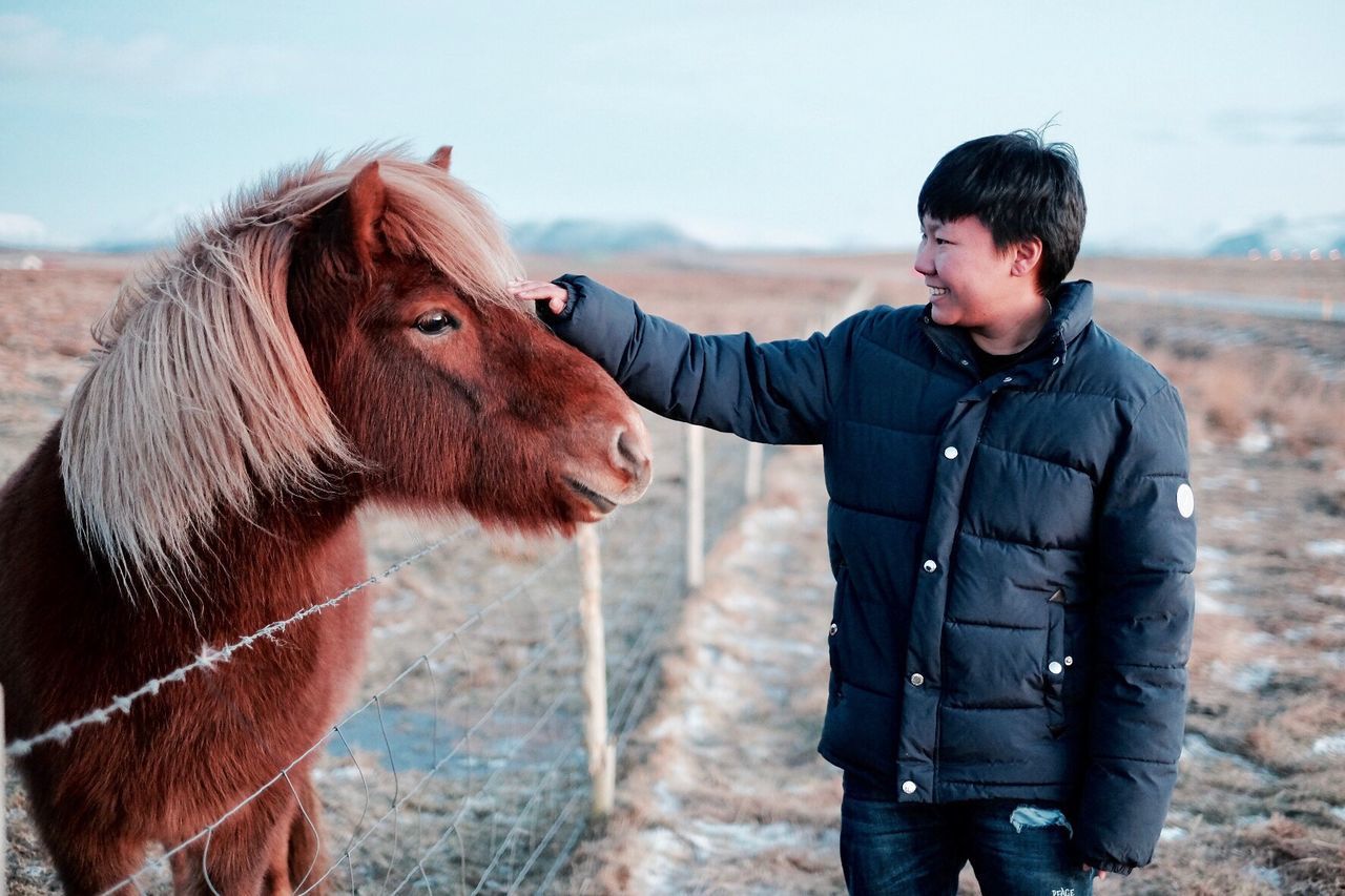 Smiling man stroking horse while standing on field