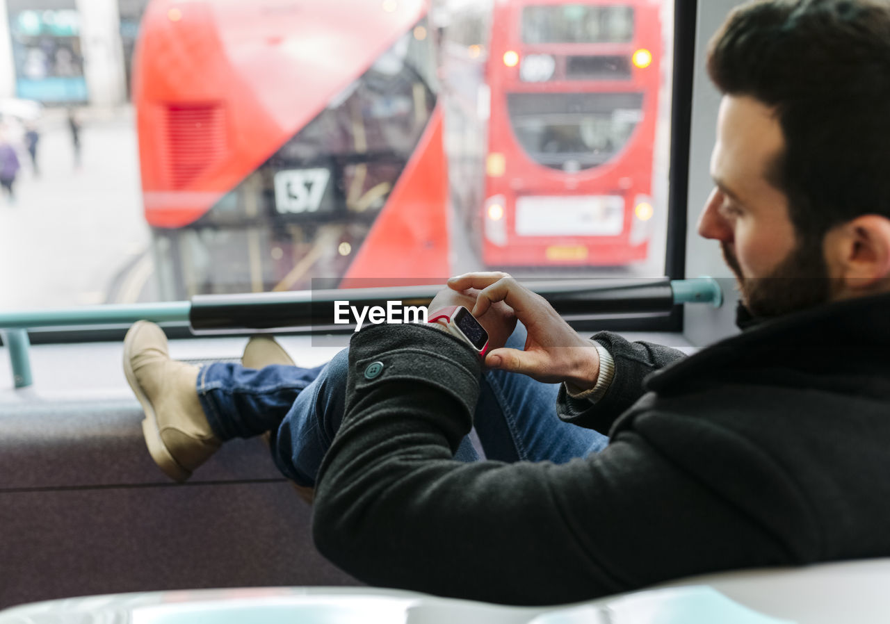 Uk, london, young man in a double-decker bus using his smartwatch