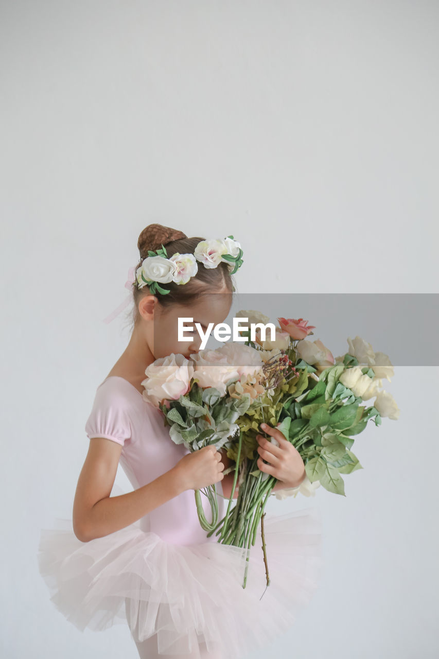 Girl wearing and holding flowers against wall