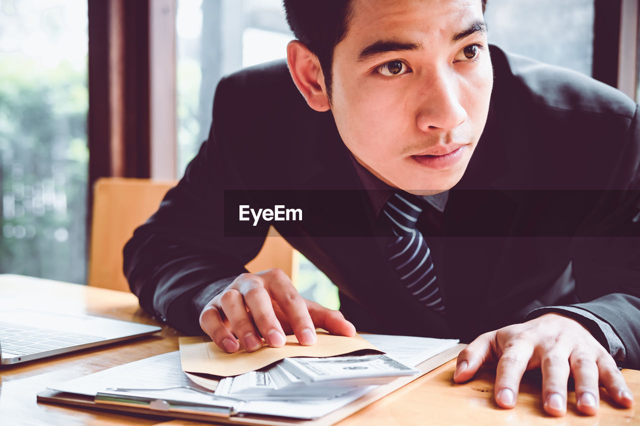 Businessman looking away while holding paper currency on table