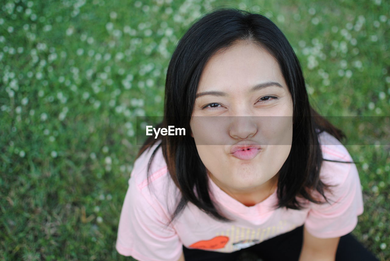 Close-up high angle portrait of playful woman puckering while sitting on grass