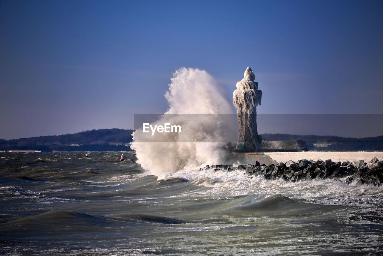 Waves splashing in sea against clear sky