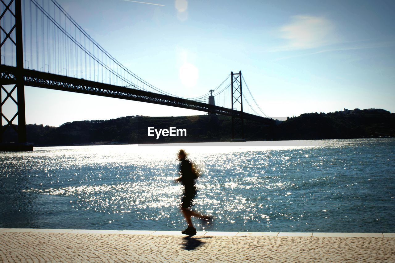 Blurred motion of man jogging by april 25th bridge over tagus river