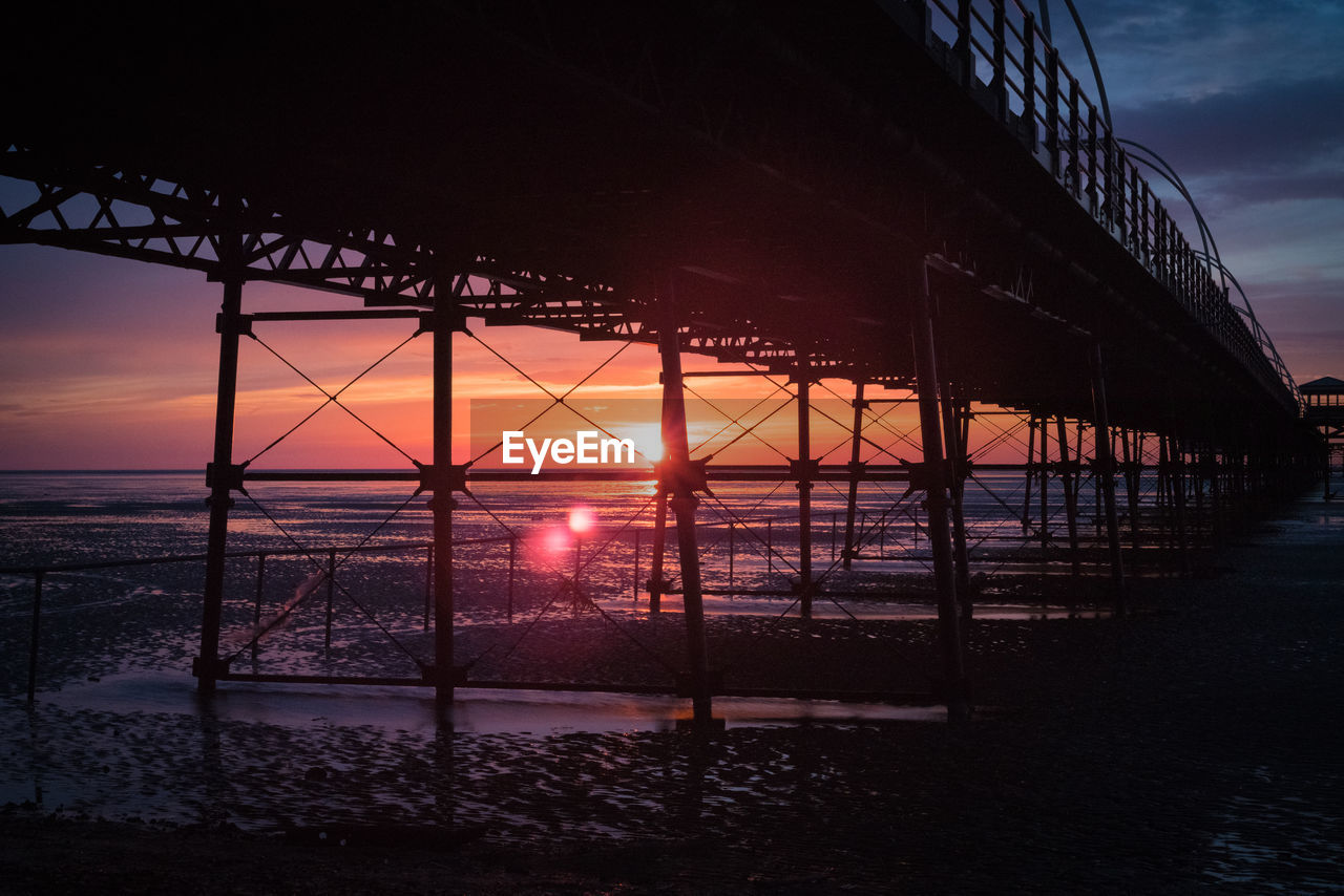 Pier at beach against sky during sunset