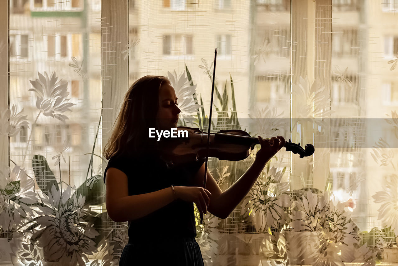 Young woman playing violin by window