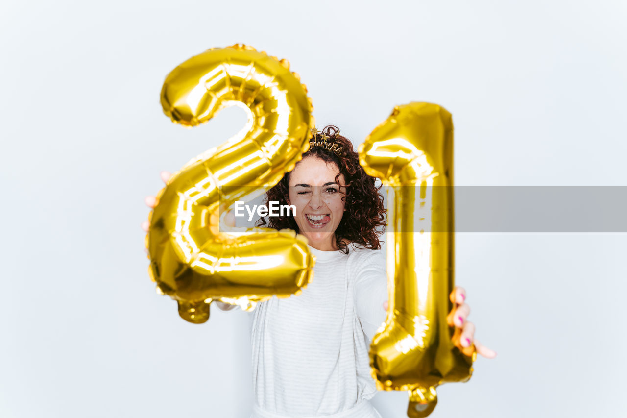 Smiling woman wearing crown holding balloons against white backgrounds