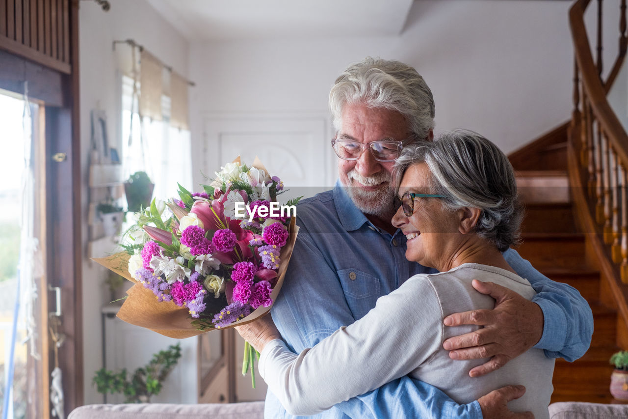 Smiling couple holding bouquet at home