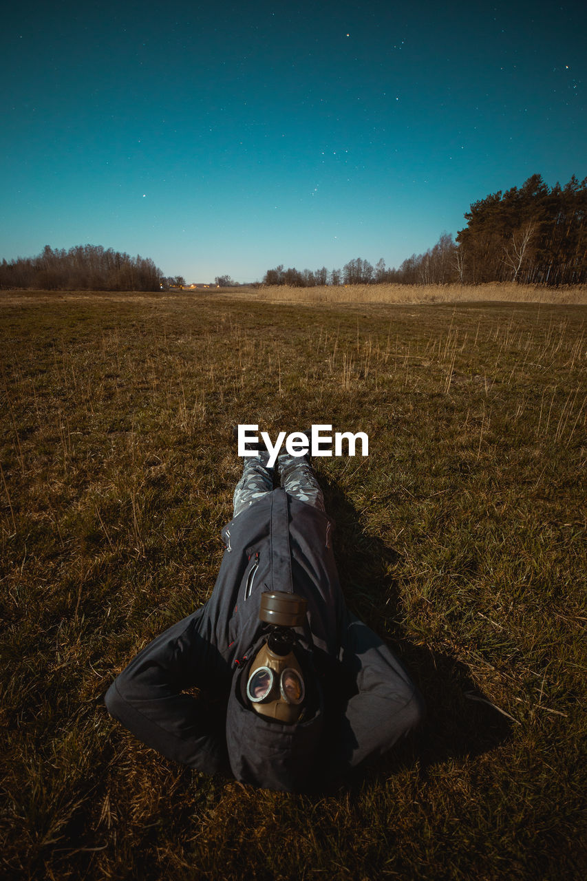 Person in the gas mask laying on the ground and watching the sky.