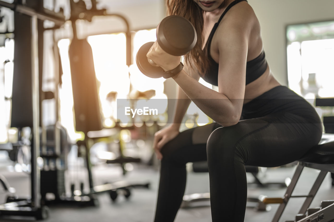 Midsection of woman exercising with dumbbell in gym