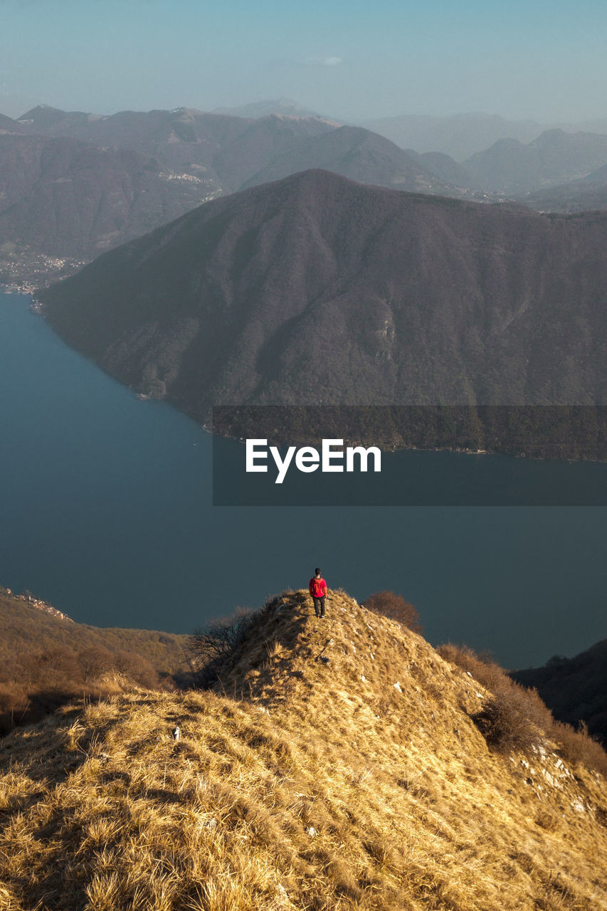 Rear view of man standing on mountain ridge looking at lake