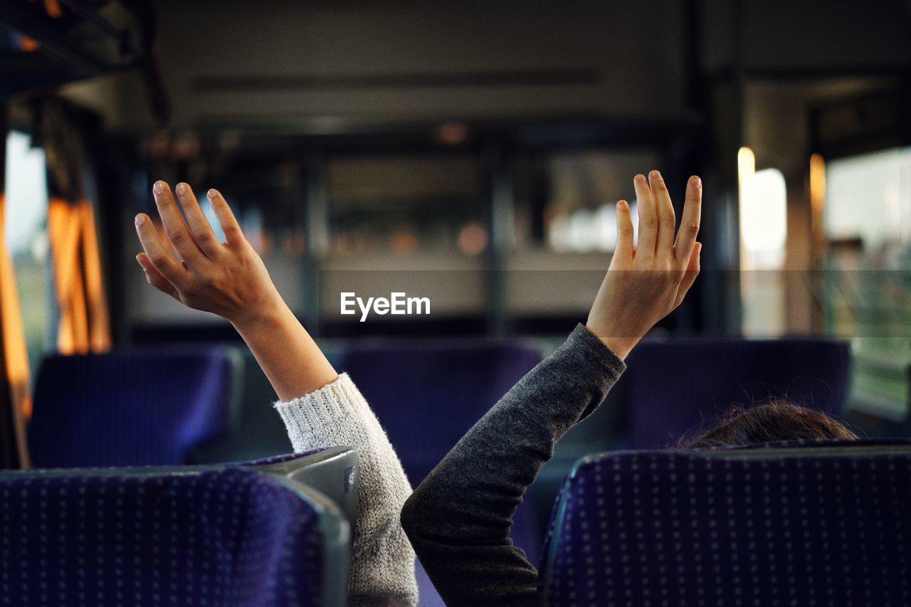 Cropped image of people with arms raised in bus