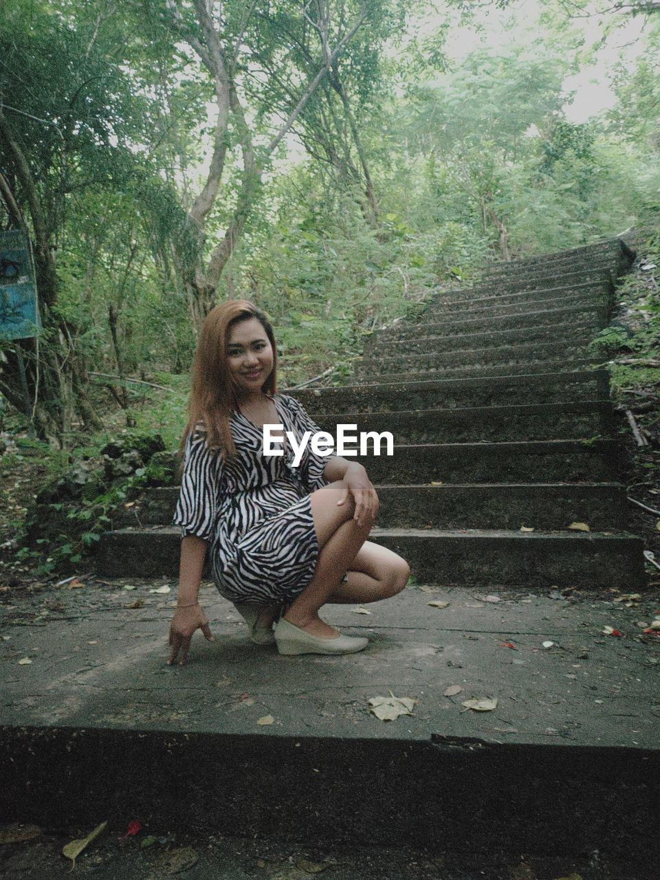 FULL LENGTH OF YOUNG WOMAN SITTING ON STAIRCASE IN FOREST