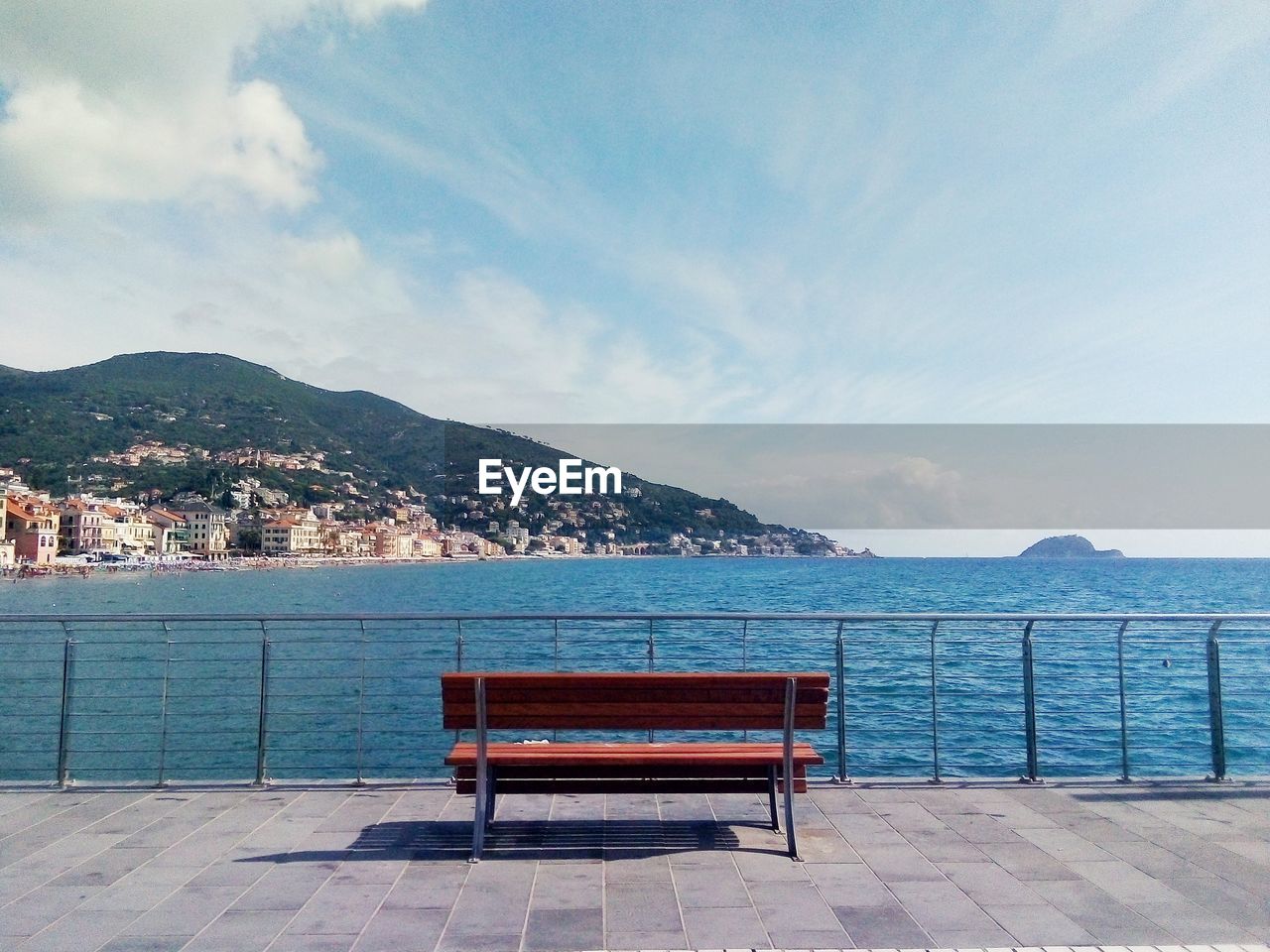 Empty bench by sea against sky