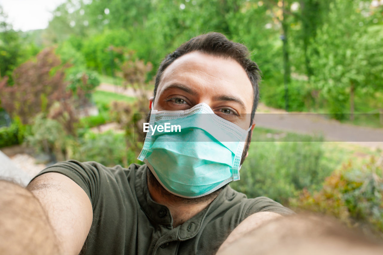 Portrait of man wearing mask standing against trees