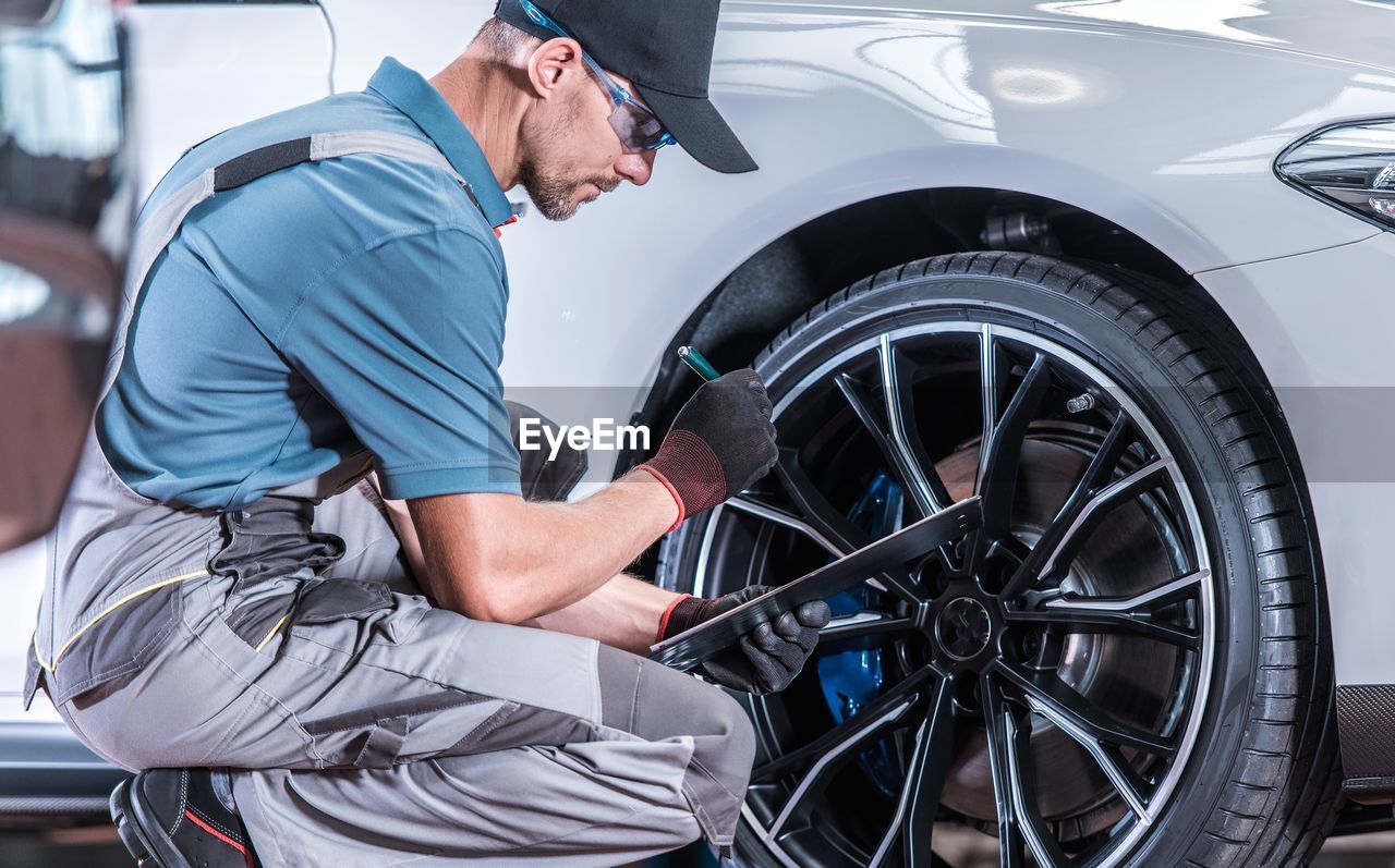 Side view of man examining car with checklist in garage