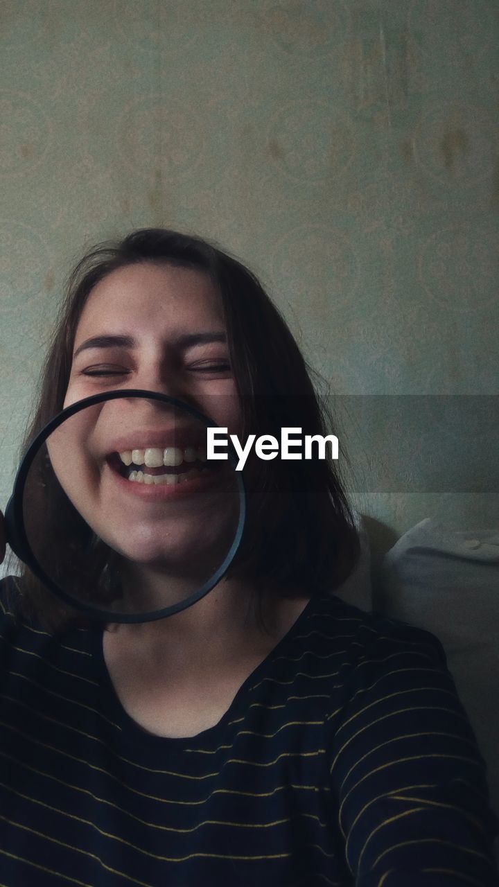 Close-up of cheerful woman with magnifying glass against wall