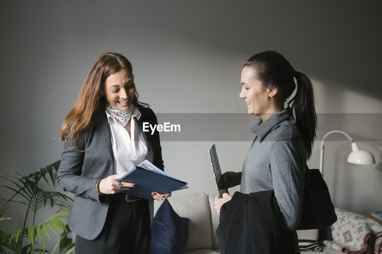 Happy woman and female realtor discussing brochure at home