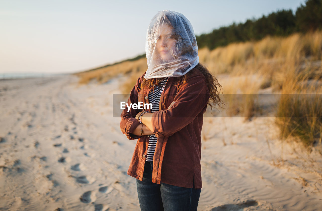 Portrait of young woman with face covered by plastic bag standing at beach