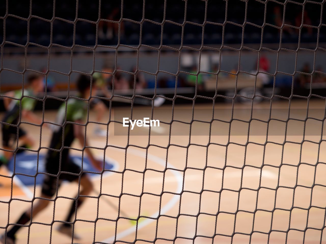 Running players in sport hall. view through the protective net of a floorball match.