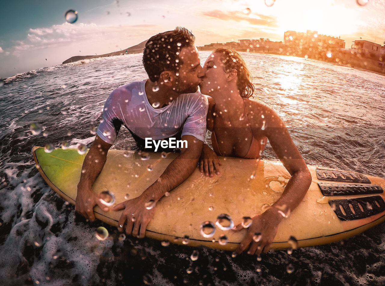 Close-up of couple kissing by surfboard in water 