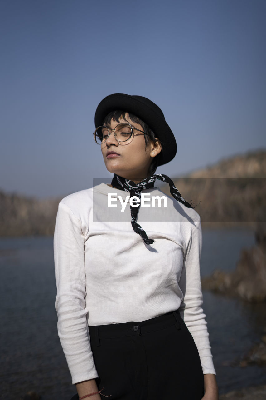 Young woman looking away while standing against sky