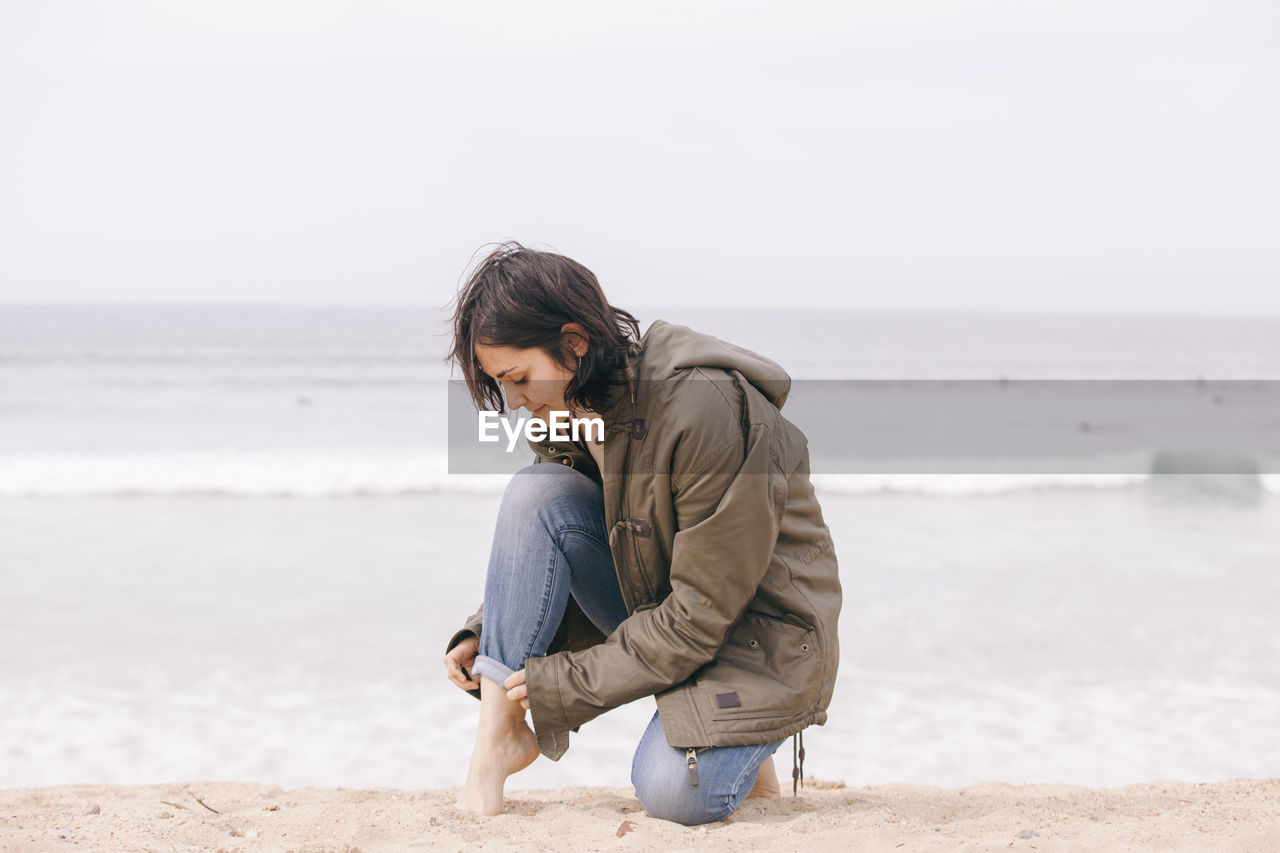 Full length of woman crouching on sand at beach