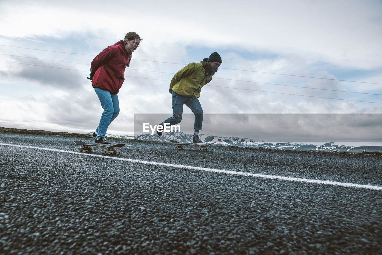 Full length of couple skateboarding on road against sky