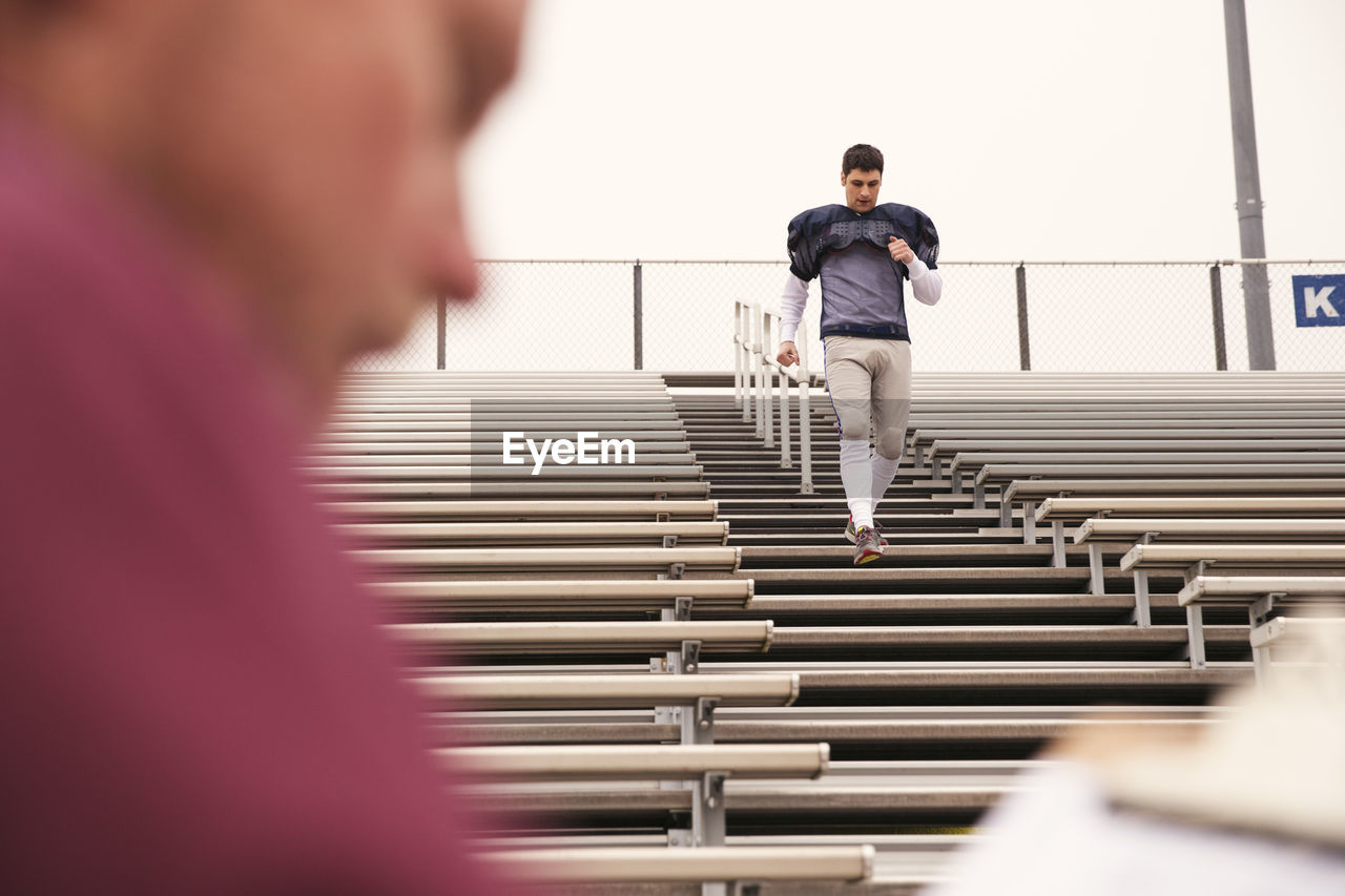 Coach holding clipboard while american football player exercising in stadium