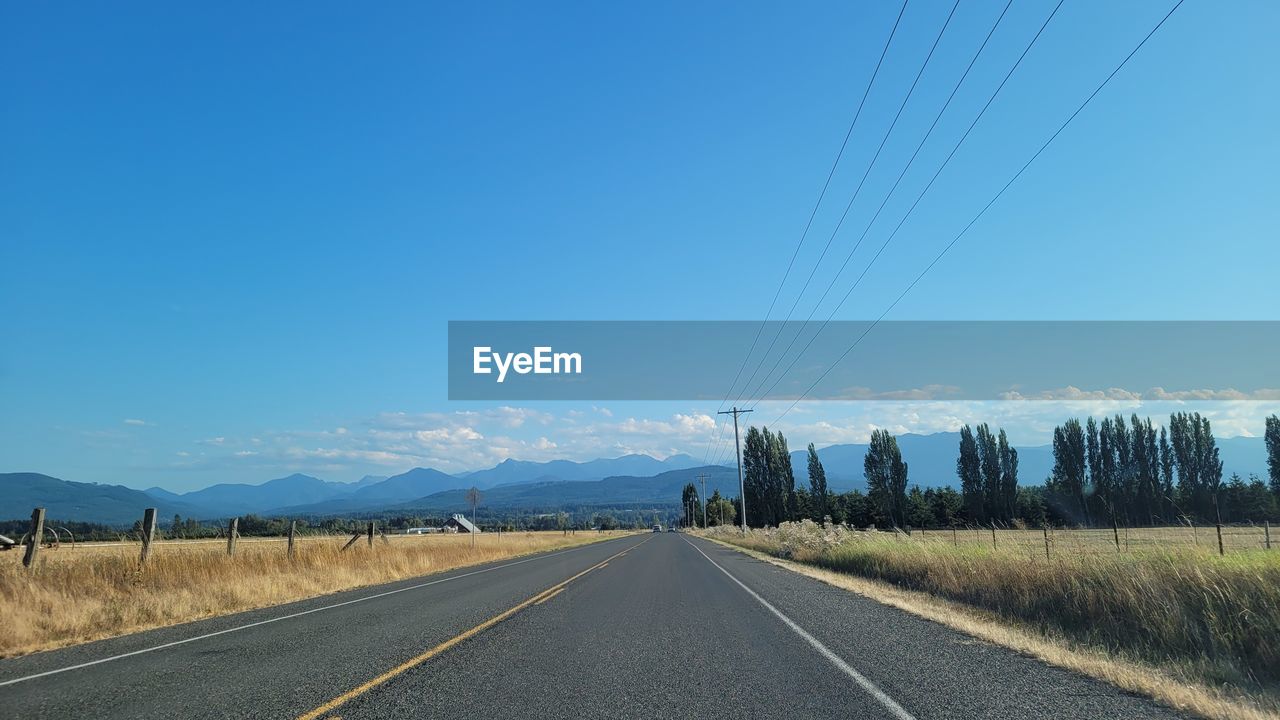 road, sky, transportation, highway, the way forward, horizon, landscape, nature, scenics - nature, blue, no people, diminishing perspective, vanishing point, mountain, environment, road marking, cable, beauty in nature, infrastructure, land, electricity, road trip, symbol, clear sky, marking, travel, sign, plant, tranquil scene, day, tranquility, non-urban scene, freeway, rural scene, tree, technology, lane, country road, outdoors, asphalt, travel destinations, remote, cloud, mountain range, street, empty road, dividing line, sunlight, power line, copy space, sunny, double yellow line