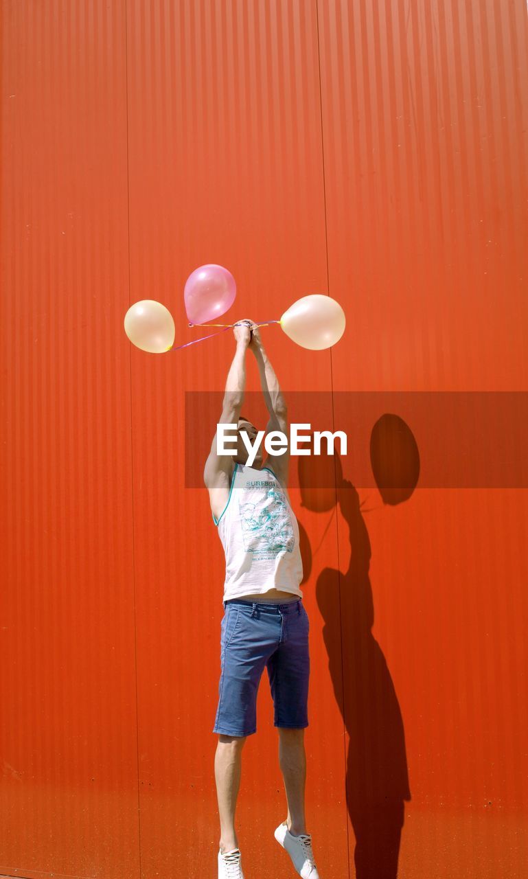 Man with balloons levitating against red wall