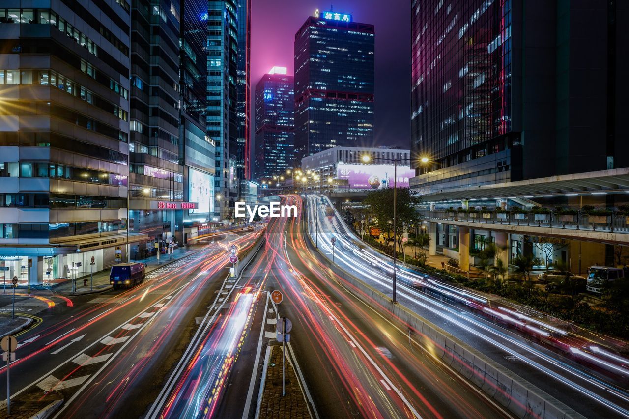 Light trails over street amidst illuminated buildings at night