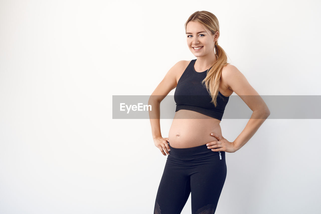 Portrait of smiling pregnant woman standing against white background