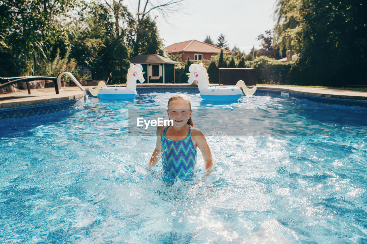Cute adorable girl swimming in pool on home backyard. kid child enjoying having fun in swimming pool