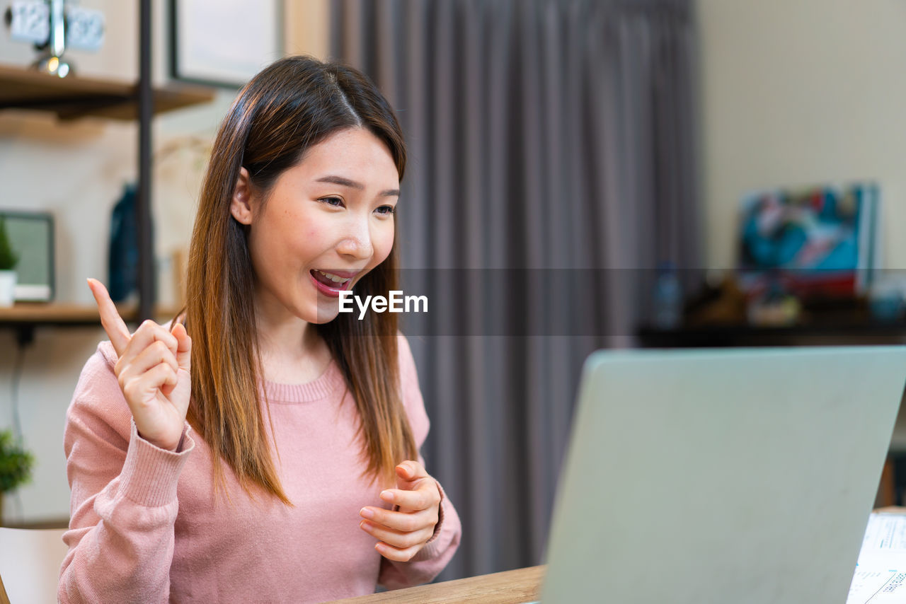 Asian woman using laptop to have video conference while working at home