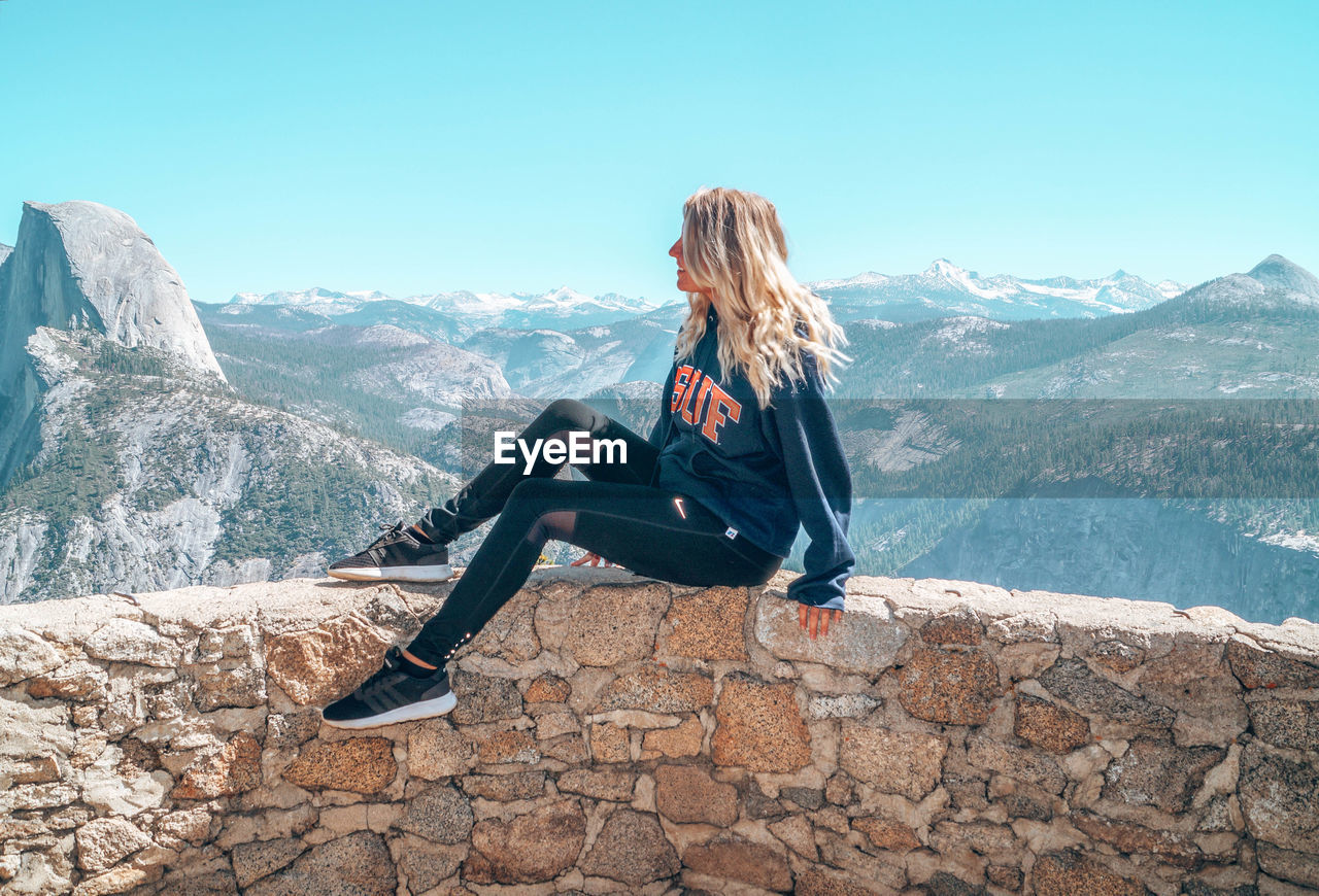 MAN SITTING ON MOUNTAINS AGAINST SKY