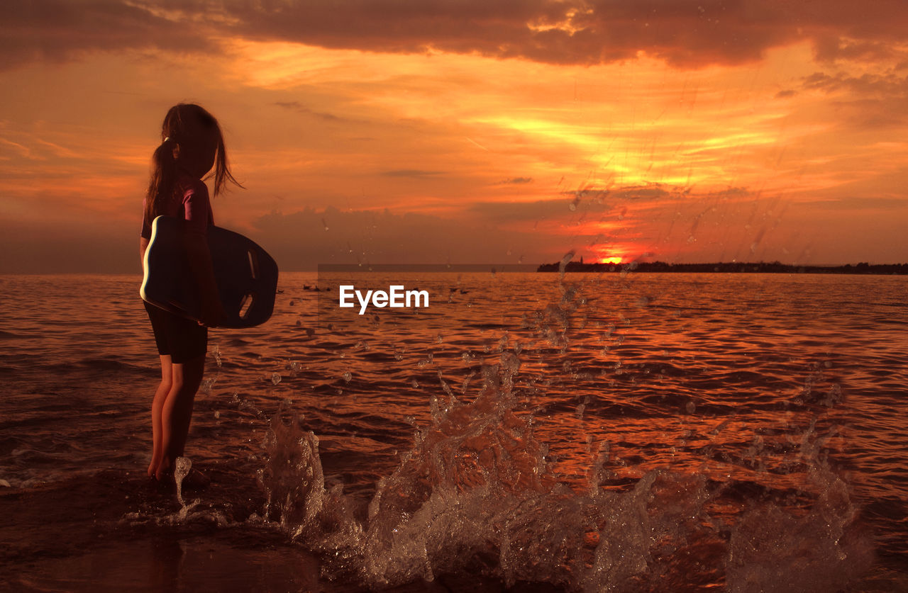 Girl standing in sea against sky during sunset