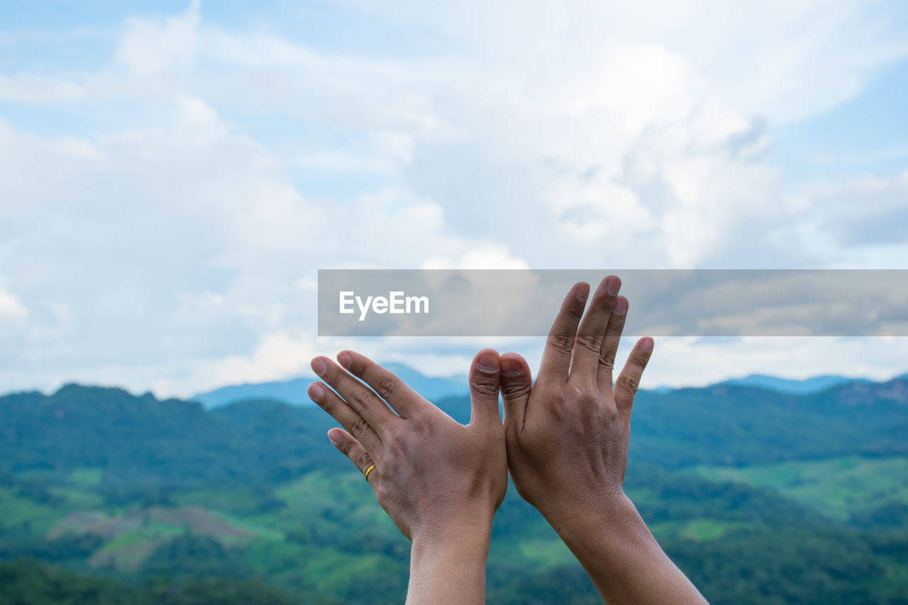 Cropped hands of person gesturing against sky