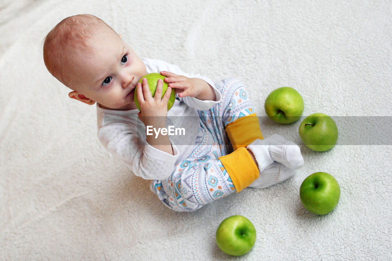 High angle view of cute baby girl sitting on carpet with apple at home