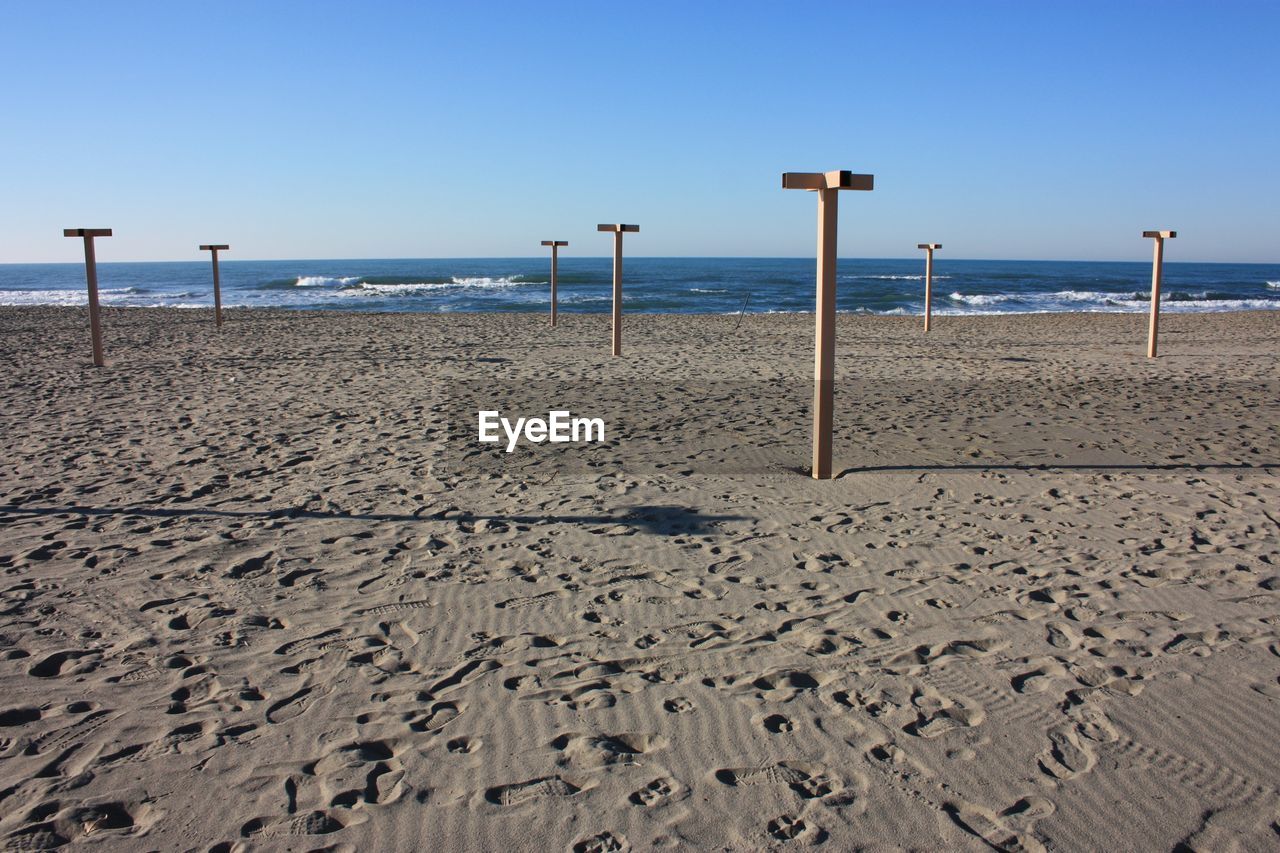 WOODEN POSTS ON BEACH AGAINST CLEAR SKY