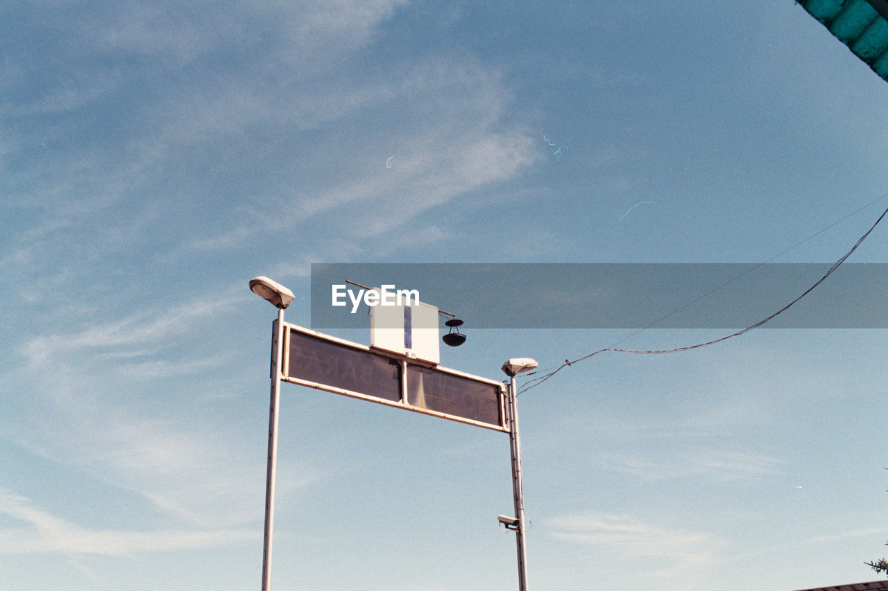 LOW ANGLE VIEW OF A BIRD PERCHING ON STREET LIGHT AGAINST SKY