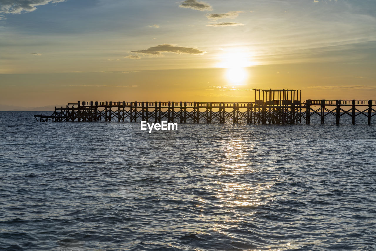 SILHOUETTE WOODEN POSTS IN SEA AGAINST SUNSET SKY