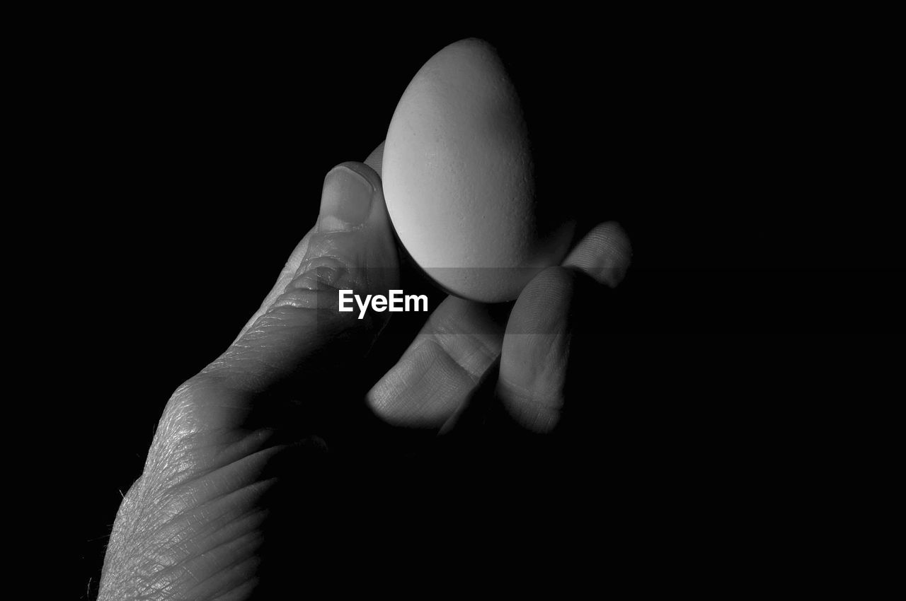 Cropped hand holding egg against black background