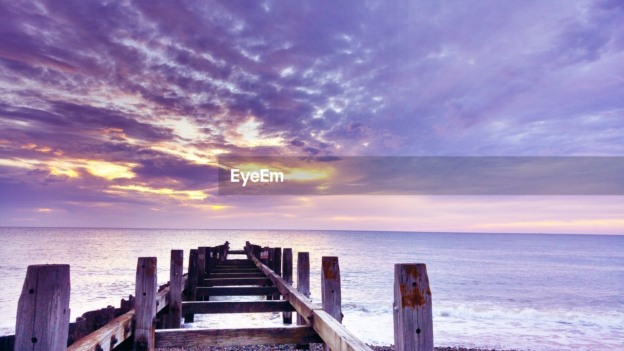 Wooden posts at beach against cloudy sky during sunset