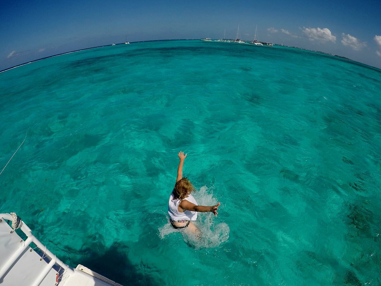 Fish-eye view of woman with arms outstretched jumping into sea