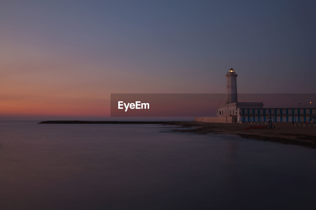 Lighthouse by sea against clear sky during sunset