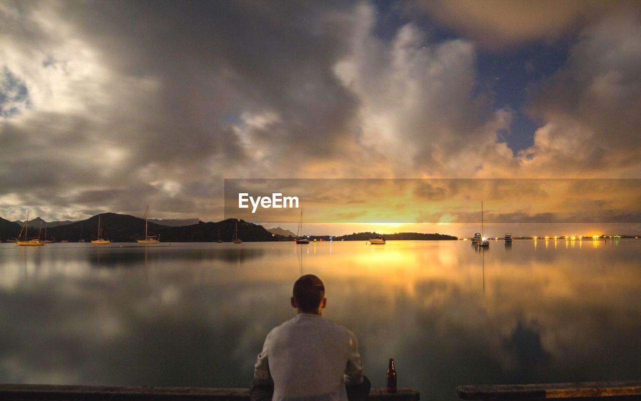 Rear view of man on lake against sky during sunset