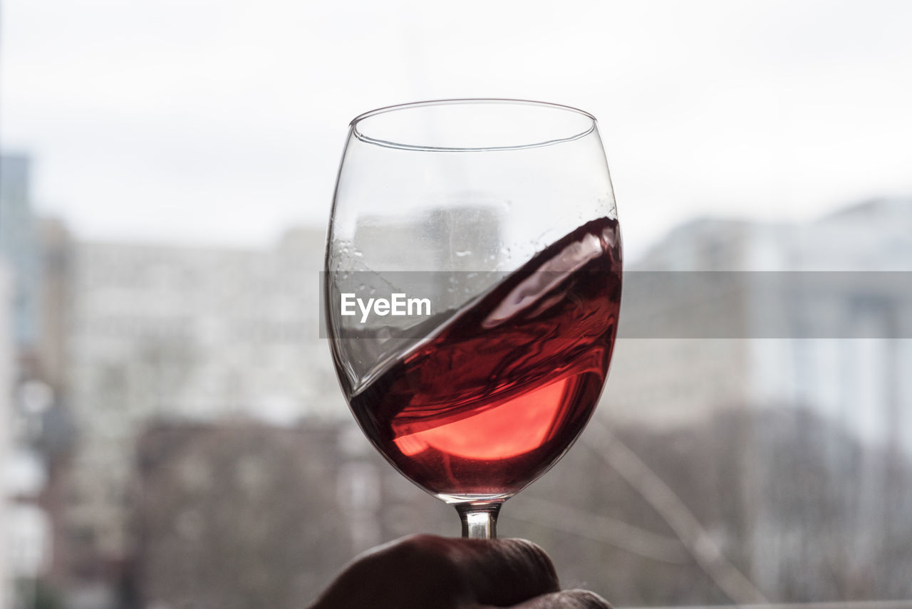 Cropped hand of man swirling wineglass against window